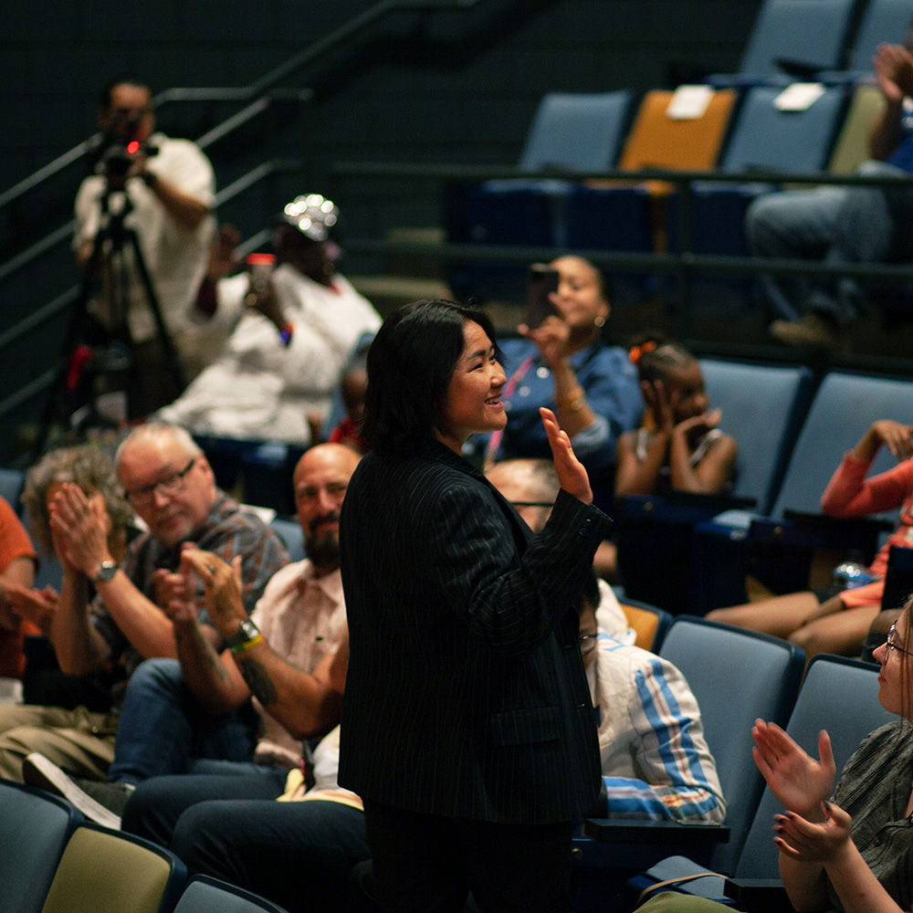 Woman standing and waving in theatre, people in seats