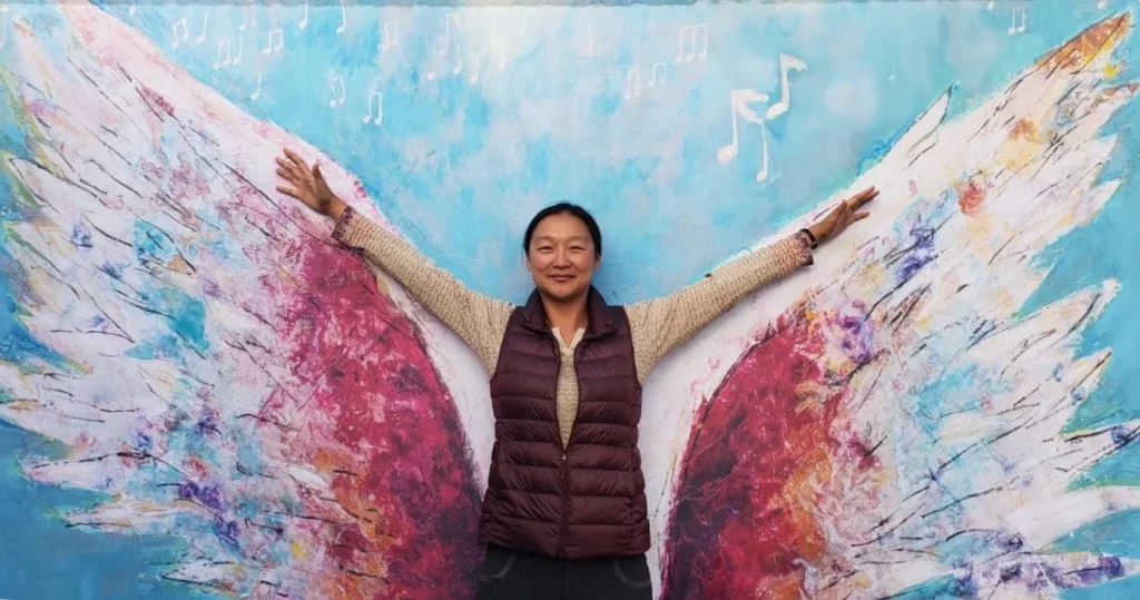 Eunice Lin Nichols holding her arms up in front of a mural painted like wings
